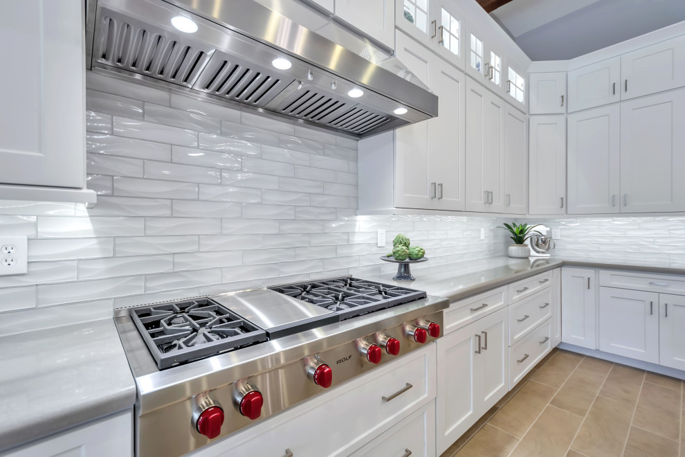 Example of a large transitional u-shaped porcelain tile, beige floor and exposed beam enclosed kitchen design in Phoenix with a farmhouse sink, shaker cabinets, white cabinets, quartz countertops, white backsplash, glass tile backsplash, stainless steel appliances, an island and white countertops