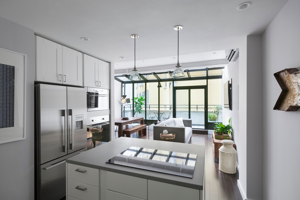 Design ideas for a mid-sized modern single-wall open plan kitchen in New York with white cabinets, stainless steel appliances, shaker cabinets, concrete benchtops, dark hardwood floors, with island and brown floor.