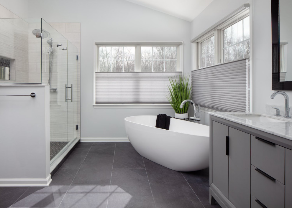 Идея дизайна: большая главная ванная комната в современном стиле с плоскими фасадами, серыми фасадами, отдельно стоящей ванной, угловым душем, раздельным унитазом, белой плиткой, керамогранитной плиткой, серыми стенами, полом из керамогранита, врезной раковиной, мраморной столешницей, черным полом, душем с распашными дверями, белой столешницей, нишей, тумбой под две раковины и напольной тумбой
