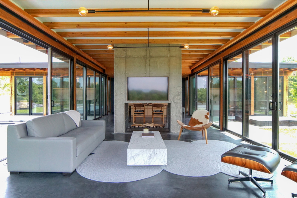 Midcentury open concept family room in New York with a two-sided fireplace, concrete floors, a concrete fireplace surround and grey floor.