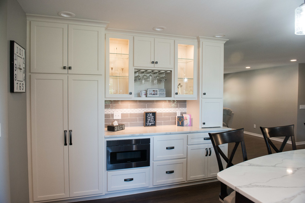 Eat-in kitchen - large transitional u-shaped laminate floor and brown floor eat-in kitchen idea with a double-bowl sink, shaker cabinets, white cabinets, quartz countertops, gray backsplash, subway tile backsplash, stainless steel appliances, an island and white countertops