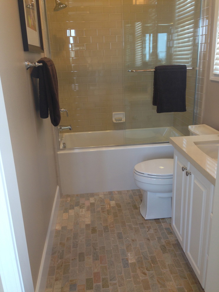 This is an example of a small traditional bathroom in Orange County with raised-panel cabinets, white cabinets, an alcove tub, a shower/bathtub combo, a two-piece toilet, beige tile, subway tile, beige walls, brick floors, an undermount sink, solid surface benchtops, multi-coloured floor and a sliding shower screen.