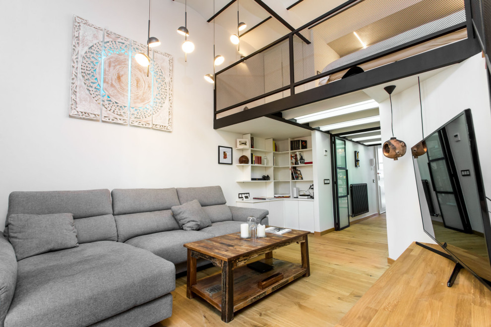 This is an example of a mid-sized industrial formal enclosed living room in Barcelona with white walls, medium hardwood floors, a freestanding tv, brown floor, vaulted and brick walls.