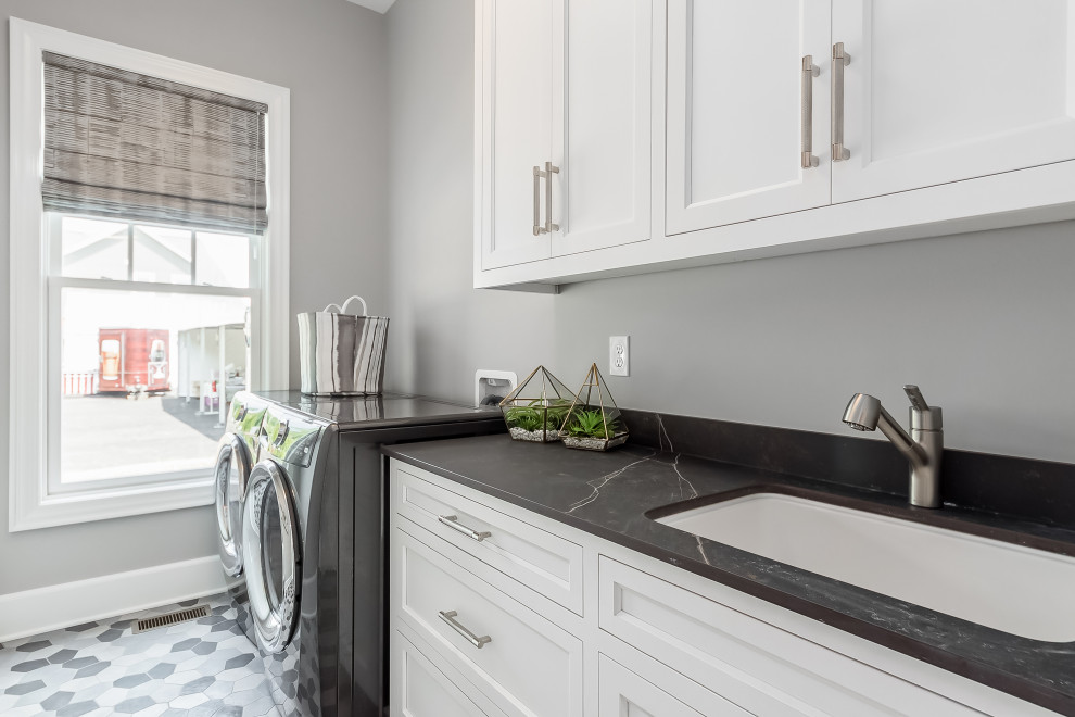 Inspiration for a large modern single-wall laundry room in Columbus with an undermount sink, shaker cabinets, white cabinets, quartz benchtops, black splashback, engineered quartz splashback, white walls, porcelain floors, a side-by-side washer and dryer, multi-coloured floor and black benchtop.