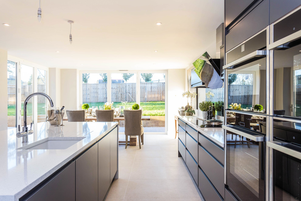 Design ideas for a mid-sized contemporary galley eat-in kitchen in Buckinghamshire with a drop-in sink, flat-panel cabinets, marble benchtops, black appliances, ceramic floors, with island and grey benchtop.