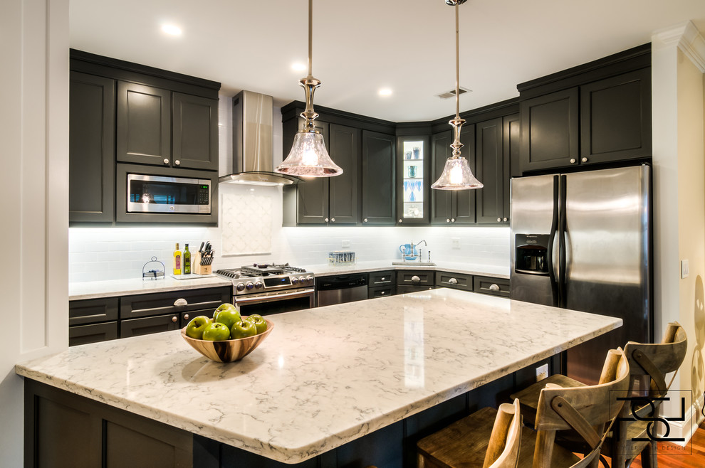 Mid-sized transitional l-shaped medium tone wood floor eat-in kitchen photo in Chicago with an undermount sink, recessed-panel cabinets, black cabinets, marble countertops, white backsplash, subway tile backsplash, stainless steel appliances and an island