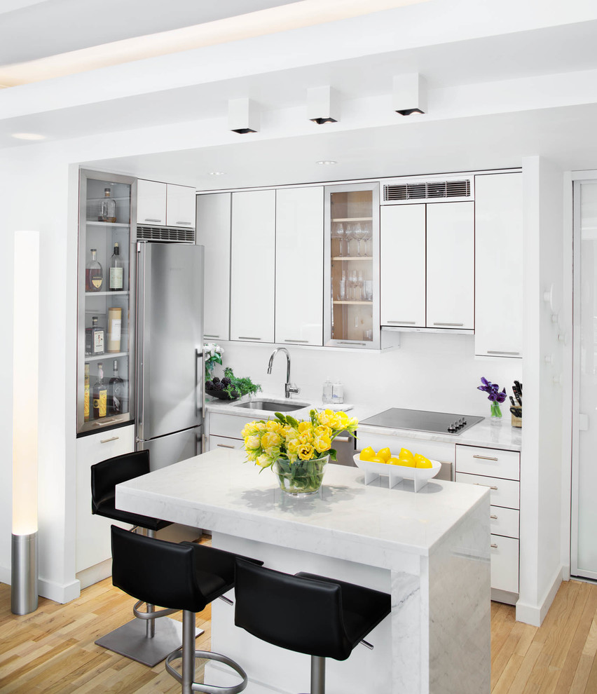 This is an example of a small modern single-wall open plan kitchen in New York with flat-panel cabinets, white cabinets, marble benchtops, stainless steel appliances, medium hardwood floors, with island, an undermount sink and yellow floor.