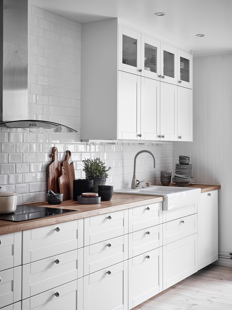 Design ideas for a scandinavian single-wall kitchen in Gothenburg with a drop-in sink, recessed-panel cabinets, white cabinets, wood benchtops, white splashback, subway tile splashback, light hardwood floors and beige floor.