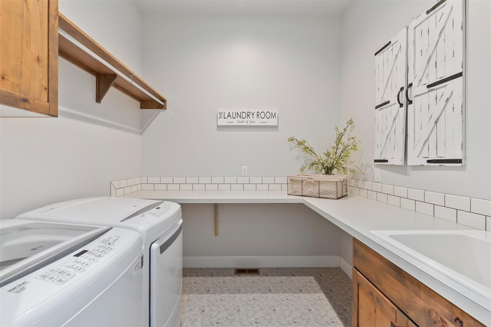 Photo of a mid-sized traditional u-shaped dedicated laundry room in Boise with an utility sink, recessed-panel cabinets, medium wood cabinets, laminate benchtops, white splashback, subway tile splashback, grey walls, laminate floors, a side-by-side washer and dryer, multi-coloured floor and grey benchtop.