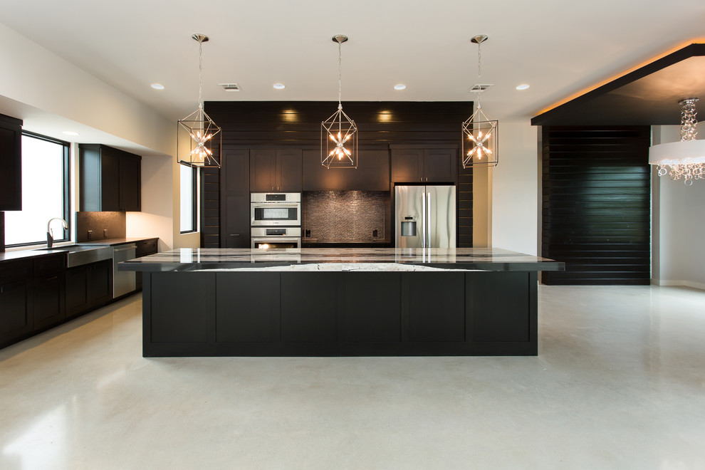 Photo of a large contemporary l-shaped eat-in kitchen in Austin with shaker cabinets, with island, black cabinets, a farmhouse sink, metallic splashback, stainless steel appliances and concrete floors.