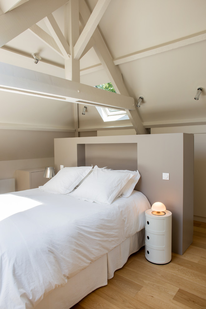 Scandinavian loft-style bedroom in Paris with beige walls, medium hardwood floors, brown floor and vaulted.