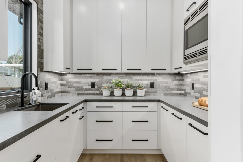Large contemporary l-shaped eat-in kitchen in Salt Lake City with a farmhouse sink, flat-panel cabinets, white cabinets, quartzite benchtops, grey splashback, stone tile splashback, stainless steel appliances, porcelain floors, with island, beige floor and grey benchtop.