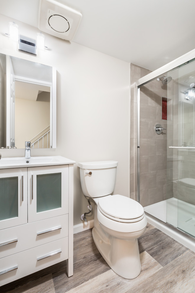 This is an example of a small transitional bathroom in DC Metro with white cabinets, vinyl floors, grey floor, furniture-like cabinets, an alcove shower, a two-piece toilet, beige tile, porcelain tile, grey walls, an integrated sink, solid surface benchtops and a sliding shower screen.