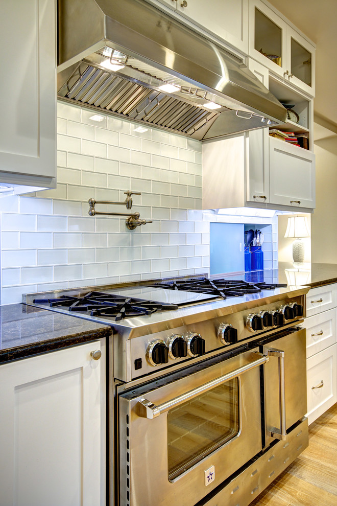 Mid-sized transitional galley light wood floor eat-in kitchen photo in Austin with shaker cabinets, white cabinets, granite countertops, white backsplash, glass tile backsplash, stainless steel appliances and no island