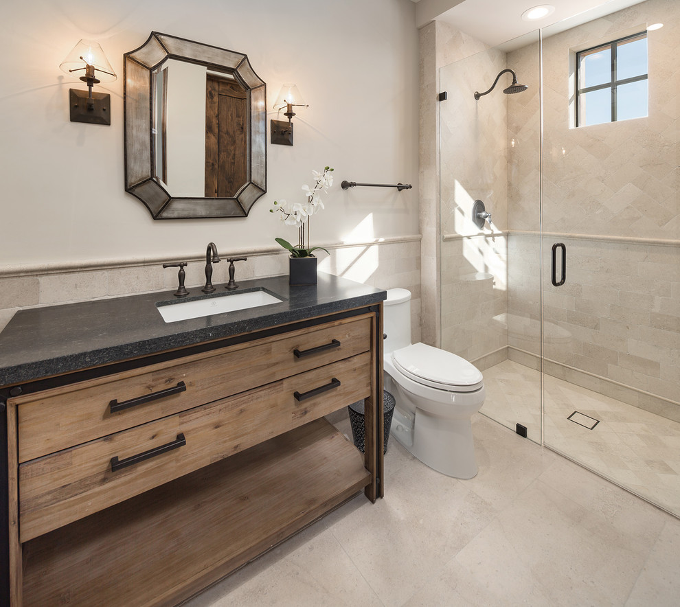 Mid-sized mediterranean 3/4 bathroom in Phoenix with flat-panel cabinets, medium wood cabinets, beige tile, beige walls, a drop-in sink, quartzite benchtops, beige floor, a hinged shower door and black benchtops.