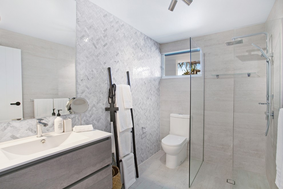 This is an example of a mid-sized beach style master bathroom in Sunshine Coast with a corner shower, a one-piece toilet, gray tile, grey walls, vinyl floors, a drop-in sink, beige floor and an open shower.
