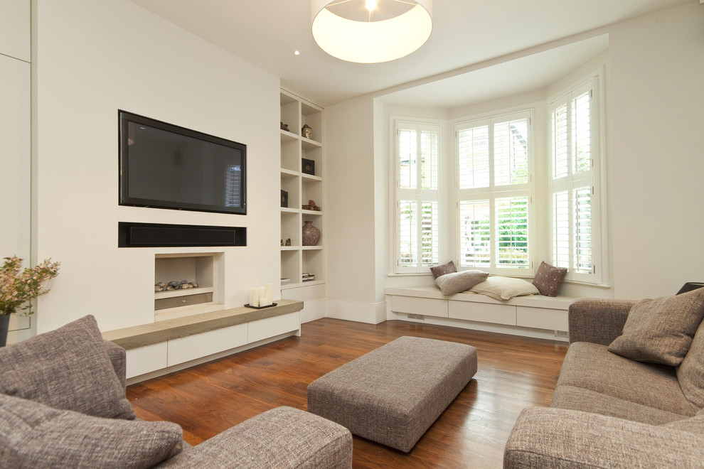 Photo of a contemporary open concept living room in London with medium hardwood floors, a standard fireplace, a wall-mounted tv and white walls.
