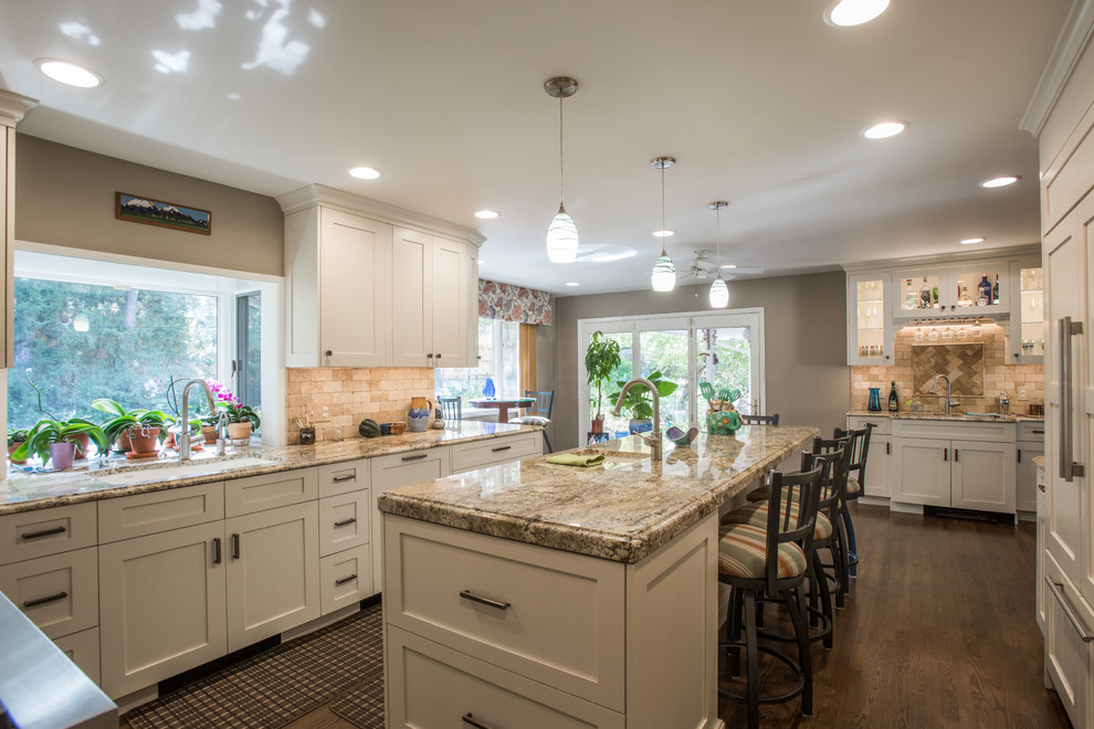 Example of a large transitional u-shaped medium tone wood floor and brown floor eat-in kitchen design with an undermount sink, shaker cabinets, white cabinets, granite countertops, beige backsplash, travertine backsplash, paneled appliances and an island
