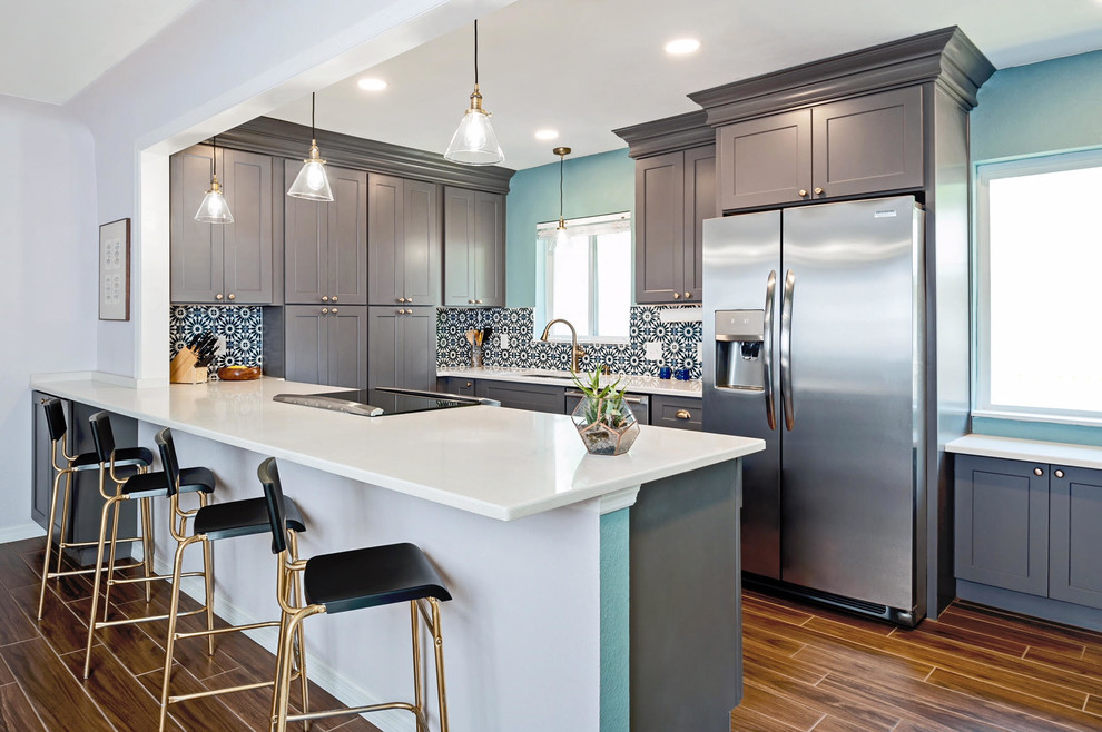 Mid-sized transitional u-shaped kitchen in Tampa with an undermount sink, shaker cabinets, grey cabinets, quartz benchtops, black splashback, stainless steel appliances, vinyl floors, a peninsula, brown floor and white benchtop.