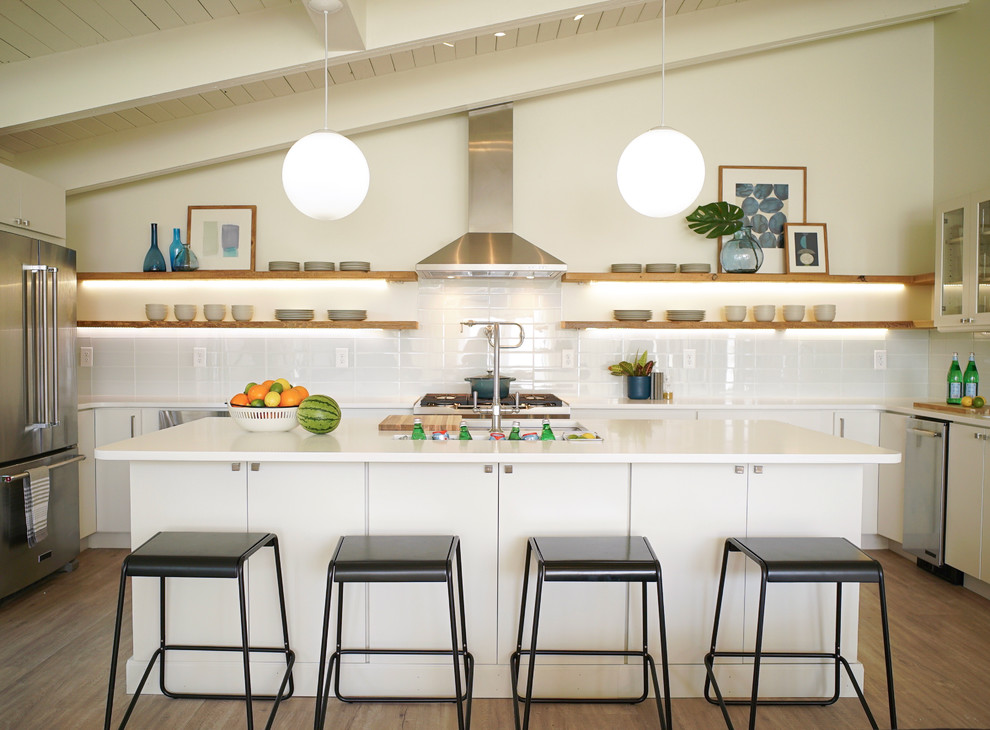 Inspiration for a midcentury u-shaped kitchen in Baltimore with an undermount sink, flat-panel cabinets, white cabinets, white splashback, stainless steel appliances, medium hardwood floors, with island, brown floor and white benchtop.