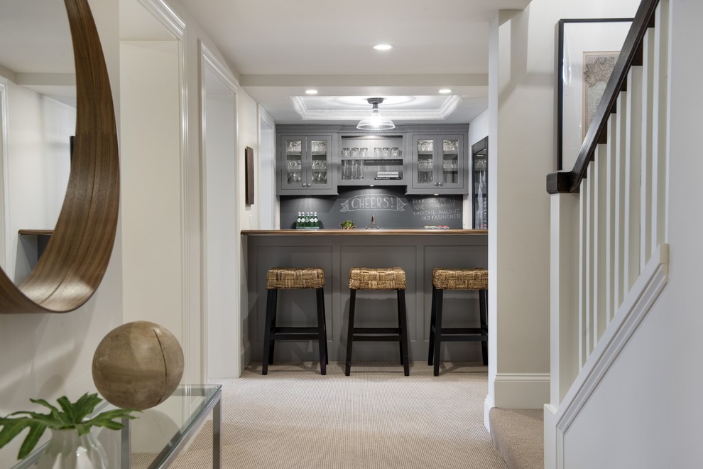 This is an example of a mid-sized transitional single-wall seated home bar in Minneapolis with an undermount sink, shaker cabinets, grey cabinets, wood benchtops, black splashback and carpet.
