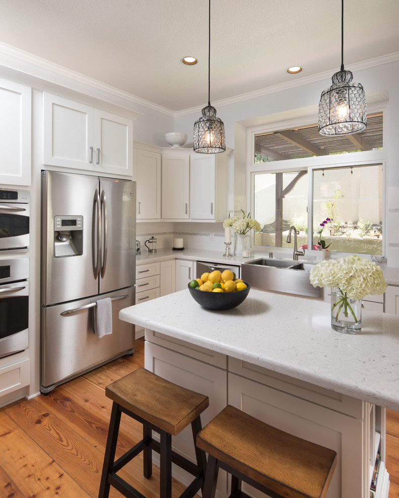 Photo of a mid-sized modern l-shaped eat-in kitchen in San Diego with a farmhouse sink, shaker cabinets, yellow cabinets, granite benchtops, white splashback, ceramic splashback, stainless steel appliances, light hardwood floors and with island.
