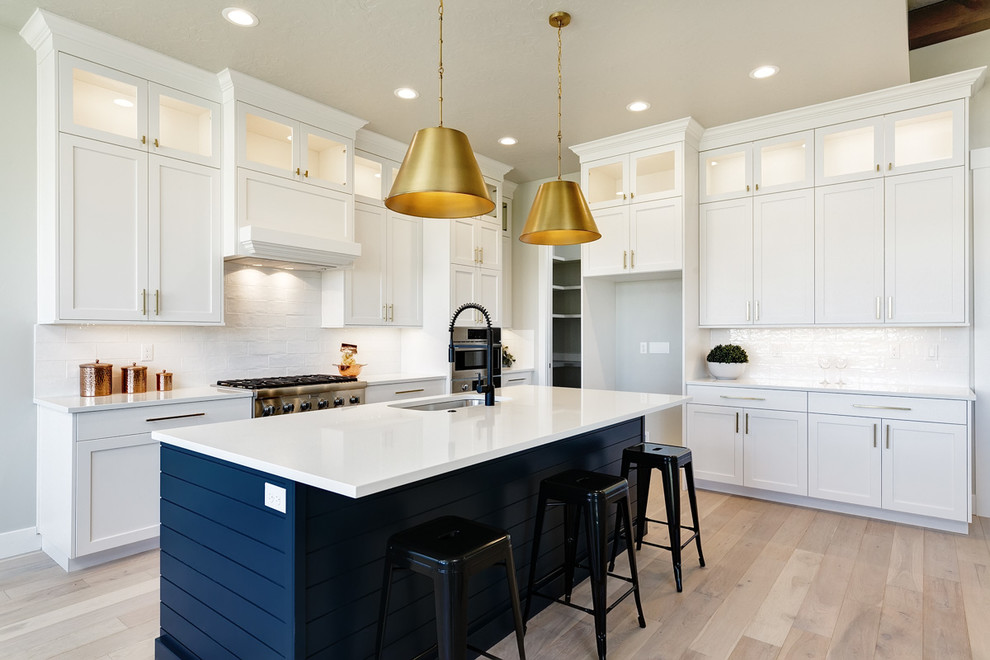 Inspiration for a large arts and crafts u-shaped eat-in kitchen in Boise with an undermount sink, recessed-panel cabinets, white cabinets, quartz benchtops, white splashback, brick splashback, stainless steel appliances, light hardwood floors, with island, beige floor and white benchtop.