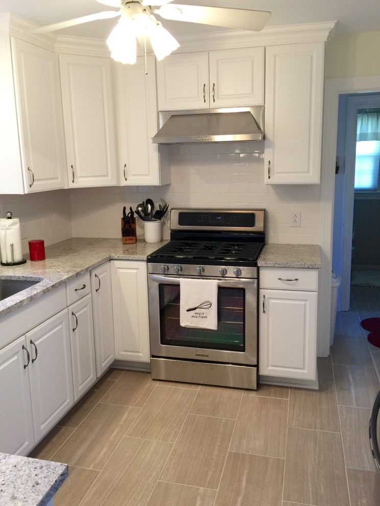 Example of a mid-sized transitional u-shaped porcelain tile enclosed kitchen design with an undermount sink, raised-panel cabinets, white cabinets, granite countertops, white backsplash, ceramic backsplash, stainless steel appliances and a peninsula