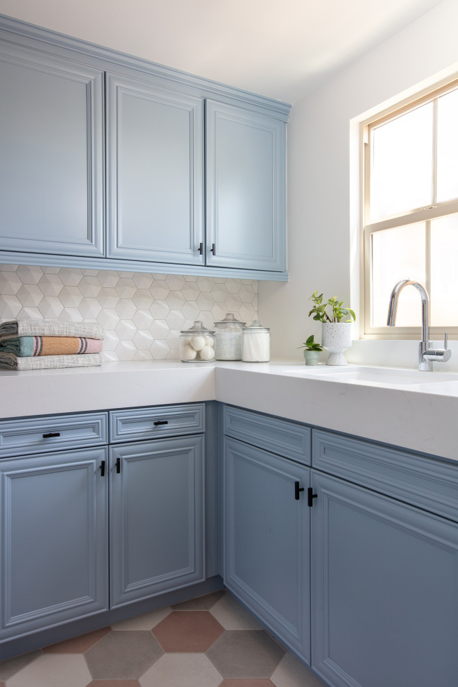 This is an example of a mid-sized modern galley laundry room in San Diego with an undermount sink, recessed-panel cabinets, blue cabinets, quartz benchtops, white splashback, ceramic splashback, white walls, porcelain floors, a side-by-side washer and dryer, pink floor and white benchtop.