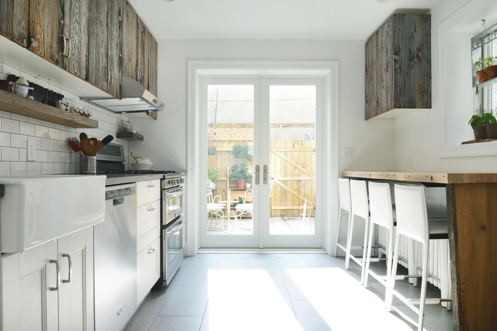 Inspiration for a mid-sized country galley eat-in kitchen in Philadelphia with flat-panel cabinets, dark wood cabinets, a farmhouse sink, wood benchtops, white splashback, subway tile splashback, stainless steel appliances, porcelain floors and grey floor.
