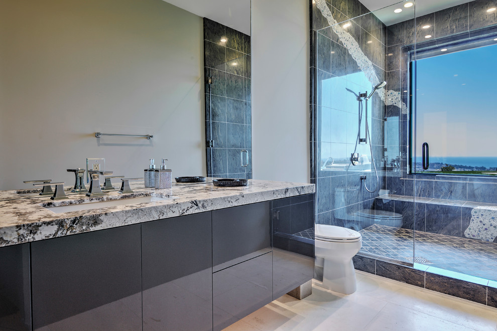 This is an example of a large contemporary master bathroom in Orange County with flat-panel cabinets, black cabinets, an alcove shower, a one-piece toilet, black tile, grey walls, an undermount sink, limestone floors and a hinged shower door.