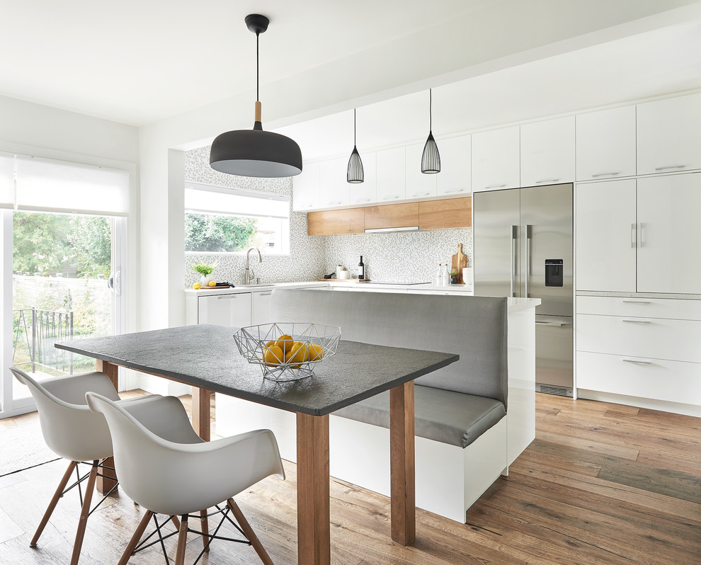 Photo of a mid-sized contemporary l-shaped eat-in kitchen in Toronto with an undermount sink, flat-panel cabinets, white cabinets, multi-coloured splashback, mosaic tile splashback, stainless steel appliances, medium hardwood floors, with island and white benchtop.