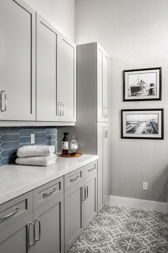 This is an example of a mid-sized beach style galley dedicated laundry room in Los Angeles with an undermount sink, shaker cabinets, grey cabinets, quartz benchtops, grey walls, porcelain floors, a side-by-side washer and dryer, grey floor and white benchtop.