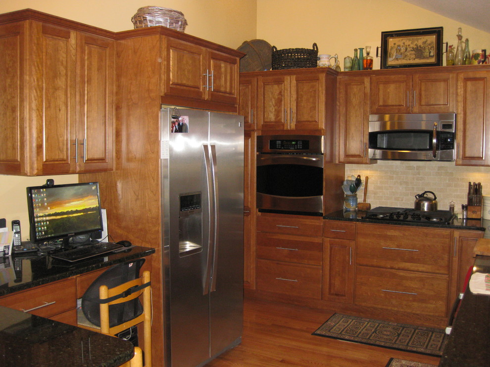 Example of a transitional u-shaped medium tone wood floor eat-in kitchen design in Boston with raised-panel cabinets, medium tone wood cabinets, granite countertops, beige backsplash, subway tile backsplash, stainless steel appliances, a peninsula, an undermount sink and black countertops