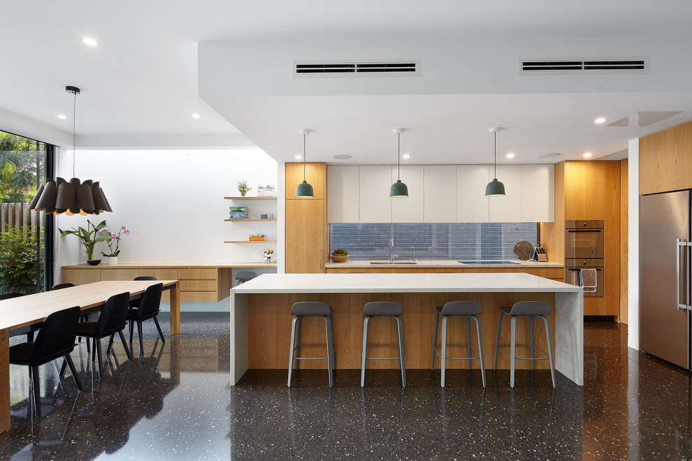 This is an example of a contemporary l-shaped open plan kitchen in Melbourne with a double-bowl sink, flat-panel cabinets, medium wood cabinets, window splashback, stainless steel appliances, with island, black floor and white benchtop.