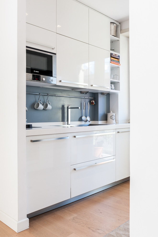 This is an example of a small contemporary u-shaped separate kitchen in Rome with white splashback, white appliances, light hardwood floors, no island, a drop-in sink, flat-panel cabinets and brown floor.