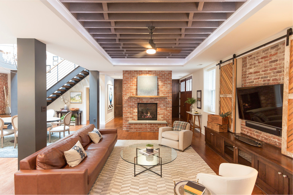 This is an example of a large industrial open concept living room in DC Metro with beige walls, medium hardwood floors, a standard fireplace, a brick fireplace surround, a wall-mounted tv and brown floor.