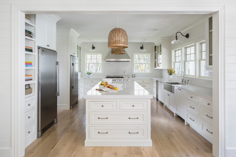 This is an example of a large country u-shaped eat-in kitchen in Minneapolis with a farmhouse sink, recessed-panel cabinets, white cabinets, quartz benchtops, white splashback, ceramic splashback, stainless steel appliances, light hardwood floors and with island.