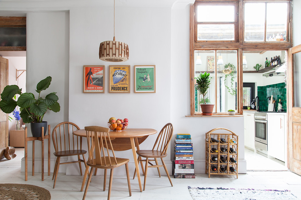 This is an example of a mid-sized eclectic open plan dining in London with white walls, painted wood floors, a standard fireplace, a metal fireplace surround and white floor.