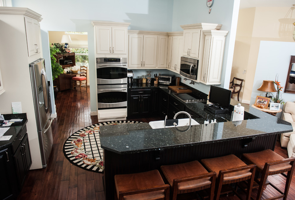 Example of a large transitional u-shaped dark wood floor eat-in kitchen design in Miami with a farmhouse sink, flat-panel cabinets, black cabinets, granite countertops, blue backsplash, stainless steel appliances and a peninsula