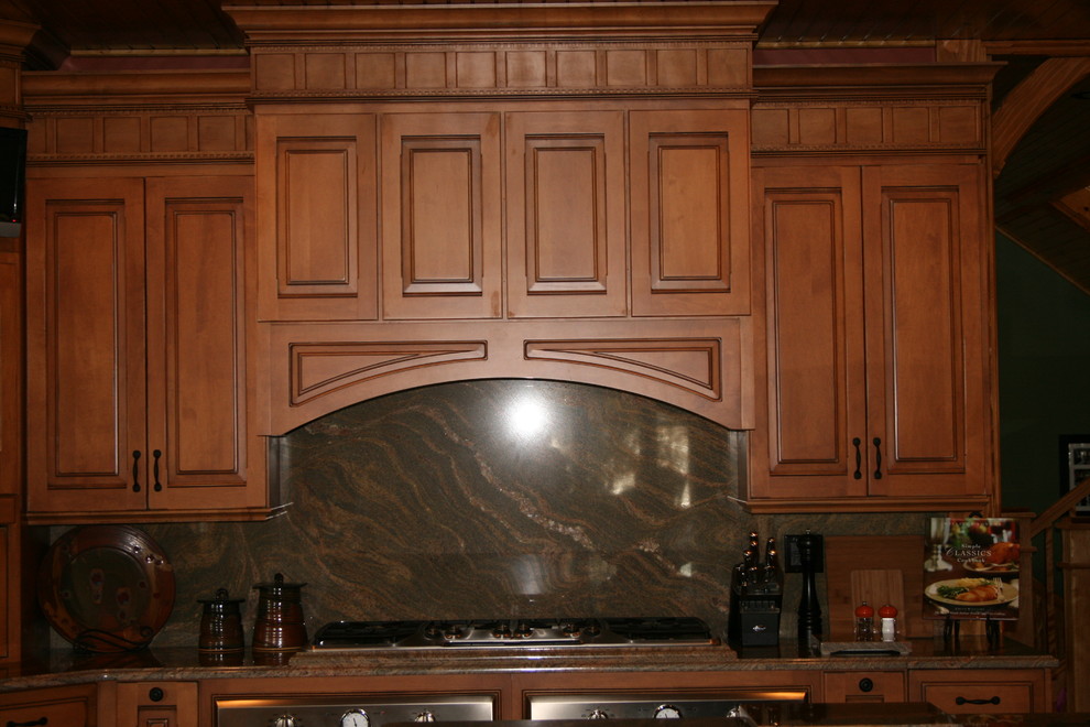 Large mountain style kitchen photo in Boston with raised-panel cabinets, dark wood cabinets, granite countertops, brown backsplash and stainless steel appliances