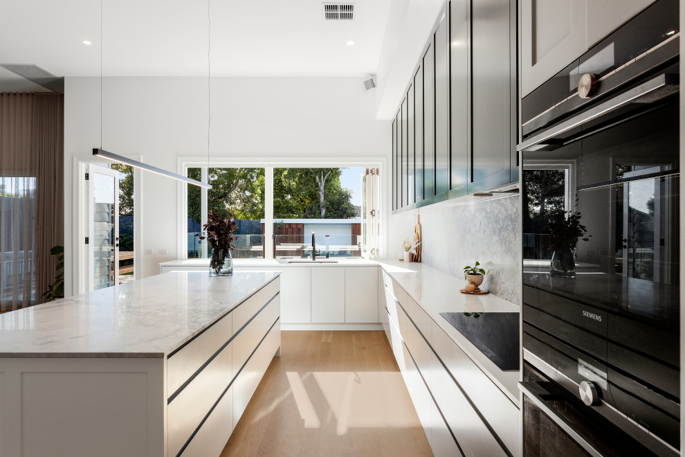 Inspiration for a large contemporary u-shaped open plan kitchen in Melbourne with a double-bowl sink, shaker cabinets, marble benchtops, grey splashback, marble splashback, black appliances, light hardwood floors, with island and grey benchtop.