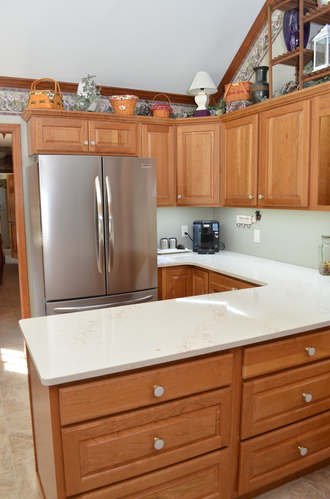 Photo of a mid-sized traditional l-shaped eat-in kitchen in Chicago with an undermount sink, raised-panel cabinets, medium wood cabinets, quartzite benchtops, stainless steel appliances, ceramic floors, a peninsula, beige floor and white benchtop.