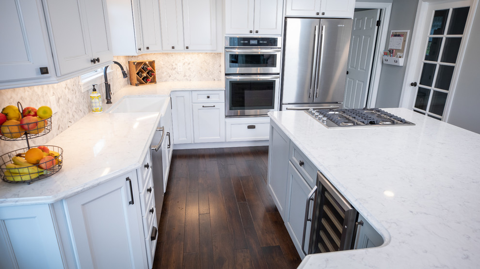 Inspiration for a large transitional u-shaped dark wood floor and brown floor eat-in kitchen remodel with a farmhouse sink, recessed-panel cabinets, white cabinets, quartz countertops, white backsplash, marble backsplash, stainless steel appliances, an island and white countertops