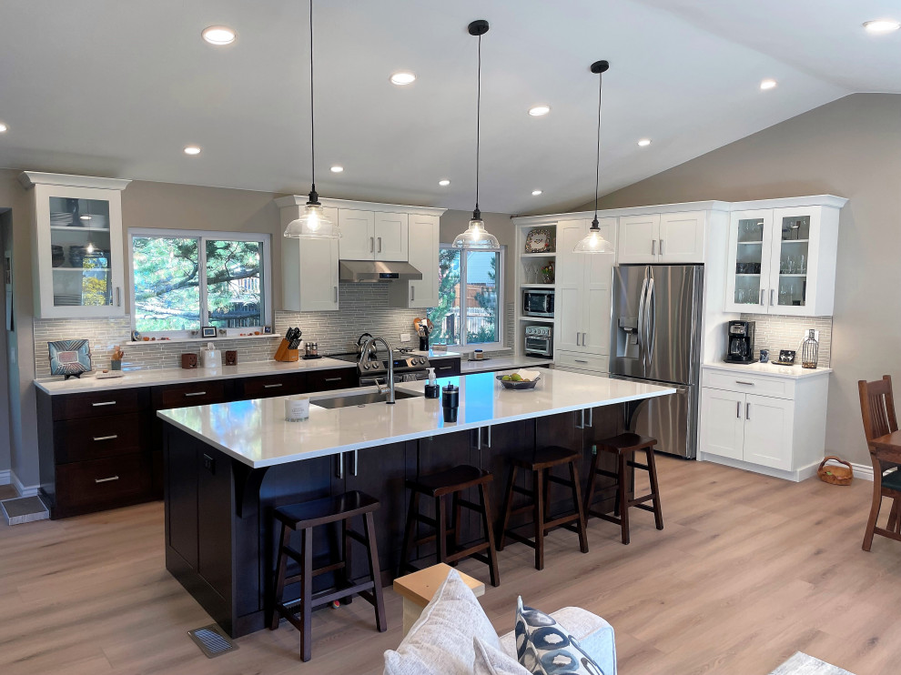 Inspiration for a large transitional l-shaped vinyl floor, beige floor and vaulted ceiling open concept kitchen remodel in Denver with a single-bowl sink, shaker cabinets, quartz countertops, gray backsplash, glass sheet backsplash, stainless steel appliances and an island