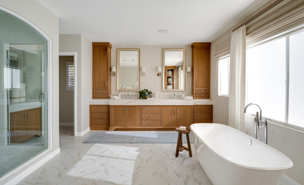 This is an example of a transitional master wet room bathroom in Orange County with brown cabinets, a freestanding tub, beige walls, marble floors, an undermount sink, marble benchtops, multi-coloured floor, a hinged shower door, multi-coloured benchtops, a double vanity, a built-in vanity and recessed-panel cabinets.