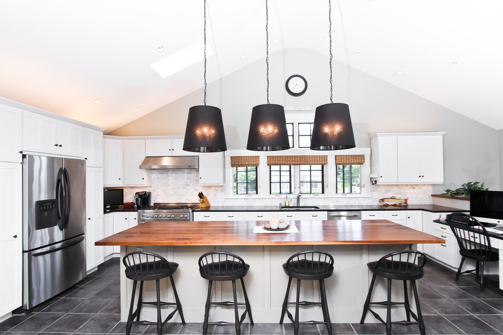 This is an example of a large transitional u-shaped eat-in kitchen in Boston with an undermount sink, white cabinets, wood benchtops, grey splashback, stone tile splashback, stainless steel appliances, slate floors, with island, shaker cabinets and grey floor.