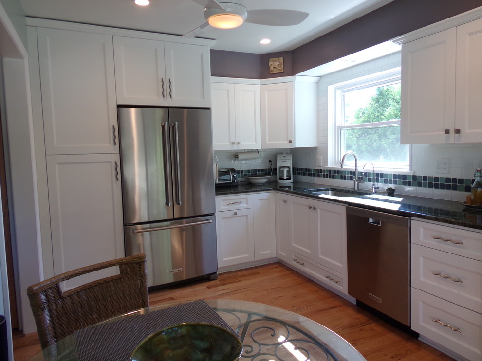 Example of a mid-sized transitional l-shaped light wood floor enclosed kitchen design with an undermount sink, flat-panel cabinets, white cabinets, granite countertops, white backsplash, subway tile backsplash, stainless steel appliances and no island