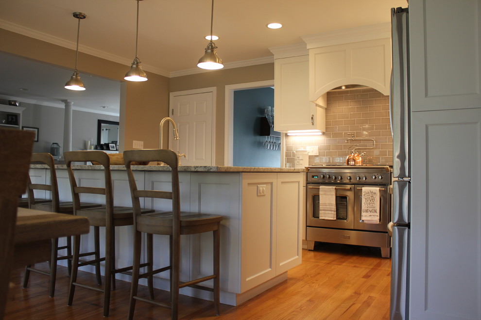 This is an example of a mid-sized traditional u-shaped eat-in kitchen in Bridgeport with a farmhouse sink, shaker cabinets, white cabinets, granite benchtops, beige splashback, porcelain splashback, stainless steel appliances, medium hardwood floors, with island, brown floor and brown benchtop.