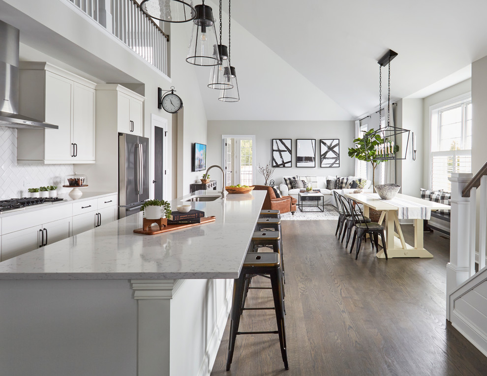 Inspiration for a beach style single-wall eat-in kitchen in Chicago with a single-bowl sink, recessed-panel cabinets, white cabinets, quartz benchtops, white splashback, subway tile splashback, stainless steel appliances, dark hardwood floors, with island, brown floor and grey benchtop.
